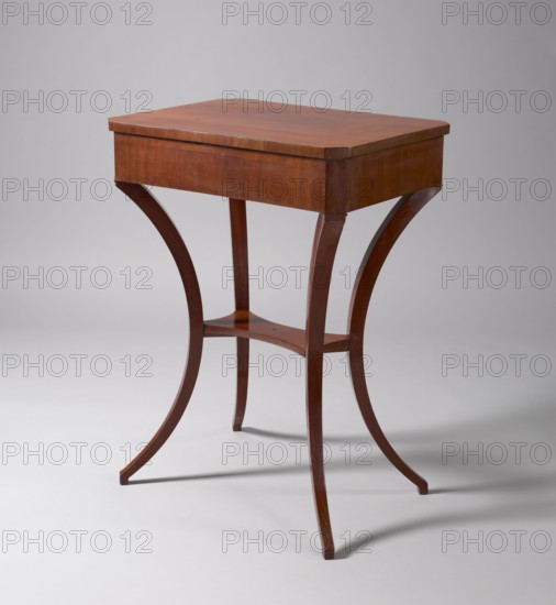 Table, classicism, gift, pre-war collection. TABLE with a rectangular top with chamfered corners, with a drawer in the frame, veneered with mahogany. Supported by four angular outward-curved legs joined mid-height by a shelf with semicircularly indented sides, originally with a finial in the middle. The chamfered corners of the frame and the outer surfaces of the legs at the top decorated with brass rosettes, the drawer lock plate is of a similar form. Mortise lock not preserved. Early 19th century, Poland, Central Europe. Furniture, table. Height 78 cm, width 57.8 cm, depth 41.5 cm., A small wooden table with a rectangular top and curved legs standing on a light gray surface against a pale gray background; the table is a warm reddish-brown wood tone with a smooth finish, showing the wood grain on the flat top and apron, and the legs curve outward into slender feet connected by a small curved stretcher of the same reddish-brown wood.
