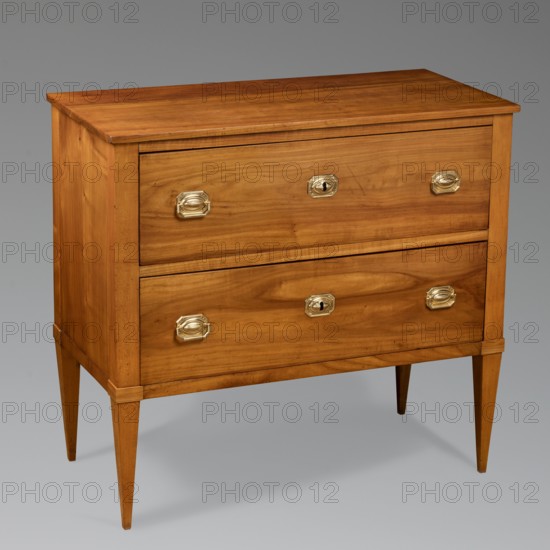Chest of drawers, Biedermeier style. Cherry, two-drawer cuboid chest on straight, tall, angular, tapering legs, polished. The body has a stand-alone structure with boarded sides and backs set in grooves; no bottom. Boarded drawer faces, recessed bottoms, with glued-on oak slides. Locks and handles of embossed brass sheet, rectangular with chamfered corners and an oval cabochon in the center; geometric cast brass pulls. Steel extruded single-bolt locks. 1820–1830, Southern Germany. Furniture storage, H 80.5 cm × W 87 cm × D 42.6 cm., A wooden chest of drawers with a warm honey-brown finish standing on tapered legs, featuring two large drawer fronts each fitted with several brass-colored oval handles and keyhole escutcheons, the wood grain visible across the top, sides, and drawer faces, and the piece set against a neutral gray background with soft shadows underneath; visible colors include brown, brass, gold, gray, and hints of darker brown in the wood grain.