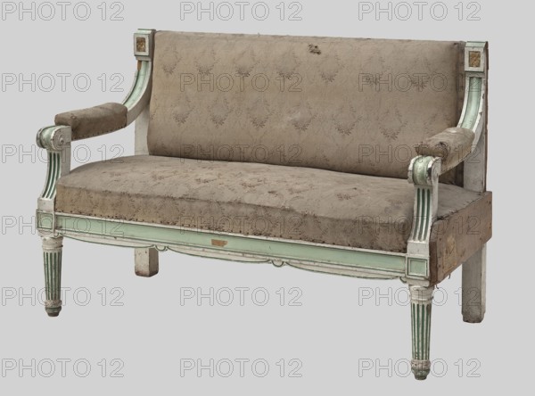 Sofa, upholstered seat, backrest, armrests, carved, lacquered white and green. Front legs turned, fluted, on round feet; rear legs angular, flowing into the side stiles of the backrest, topped with cubes with rosettes. Rectangular seat, upholstered on springs. Straight frame, wavy-cut at the bottom, with cubes above the front legs. Upper backrest stile covered with upholstery. Arched armrests at the connection with the side stiles of the backrest, volute-shaped at the front, on angular, arched-concave and fluted supports at the front. The stiles, the fields in the center of the upper surface of the armrests, and the rosettes in the cubes of the backrest stiles are lacquered green. Green paint marks the edges of the frame elements. The whole is upholstered with a cotton jacquard fabric with floral garlands. Early 20th century, Central Europe; possibly East Prussia. Seating furniture; height 96 cm, width 139 cm, depth 66 cm., A worn upholstered settee with a patterned fabric in a muted b...