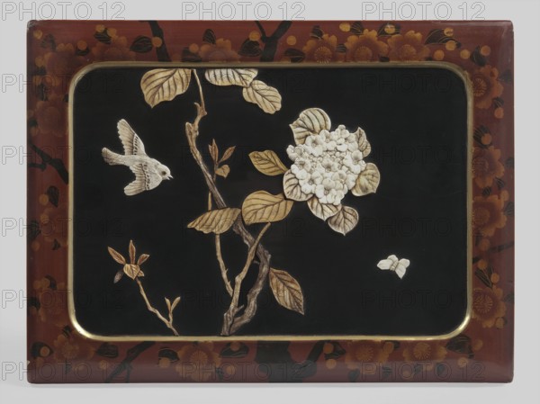 Box, Rectangular box with put-on lid, decorated with red lacquer painted with a pattern of blooming cherry blossoms. On the lid, a slightly concave black field with rounded corners, with a narrow gilded frame, inlaid carved decoration composed of hydrangea branches, a bird, and a butterfly. The branches and leaves are dyed green. Inside, four small boxes with lids, decorated with red lacquer painted with a pattern of cherry blossoms and branches. 19th/20th century, Japan. Container; height 8 cm, width 26 cm, depth 19 cm., A rectangular decorative panel with a dark central field bordered by a reddish-brown frame decorated with floral motifs in darker and golden tones; within the dark field a branch with textured bark and a few leaves rendered in beige and brown extends upward and outward, bearing a cluster of pale cream flowers with layered petals; to the left of the branch a small bird in light beige with detailed wing feathers appears in flight, and a small pale insect or moth is visi...