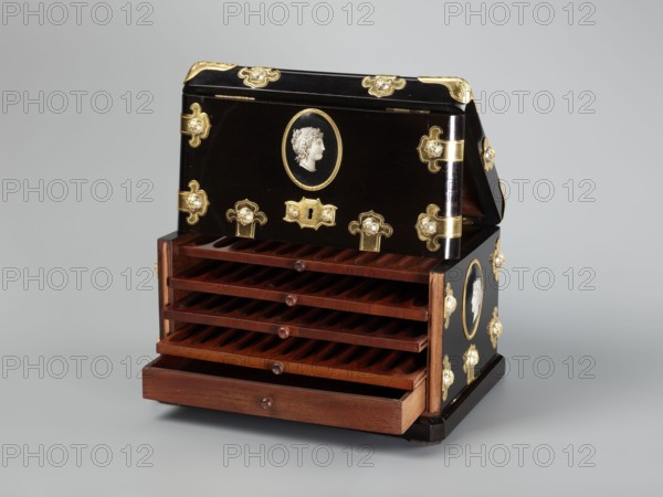 Cigar box, cigars, cameos, antiquing style, smoking tobacco, female busts, male busts, 3rd quarter of the 19th century, France, container; height 18.7 cm, width 28.5 cm, depth 20 cm, A decorative box with a glossy black exterior and a wooden interior is shown open to reveal a few wooden slatted shelves and a wooden drawer, the box is ornamented with several gold-colored metal fittings and medallion-like oval cameos bearing a profile relief in a light color, and the visible colors in the image include black, brown, gold, white, and shades of gray in the background.