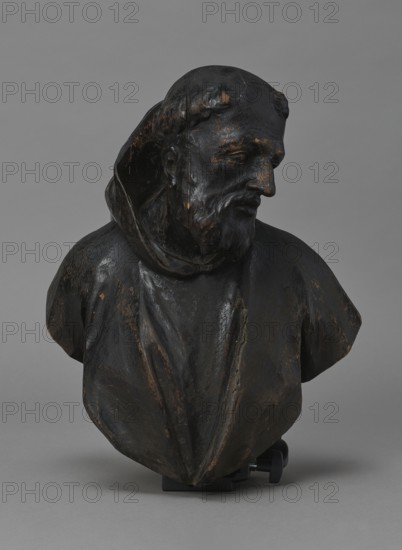 Bed finial from the Hospital of St. John of God in Warsaw, Redler, Jan Chryzostom 1704–1779 woodcarver; author, Fontana, Jakub 1710–1773 designer; co-creator, baroque; HOSPITAL BED FINIAL in the form of a pediment with volutes on the sides and a corbel in the middle supporting the bust of a monk; fastened with two pins to the front section of the cornice crowning the canopy. Figure dressed in a habit, with head turned to the left, with tonsure and beard. Outline of the finial and corbel highlighted with a black ribbon stucco inlay. On the corbel, an oval hole filled with a wooden, rotating medallion with inlaid letters on the obverse and reverse missing; above it, inlaid number No. i3. On the runners are garlands made of ribbons, flowers, and acanthus leaves; on the volutes are small brackets with turned, cup-shaped pinnacles. Ca. 1757–1760, Warsaw. Fragment of furniture; height 69.5 cm, width 91 cm, depth 24 cm., A dark wooden bust showing a robed figure turned slightly to one side, w...