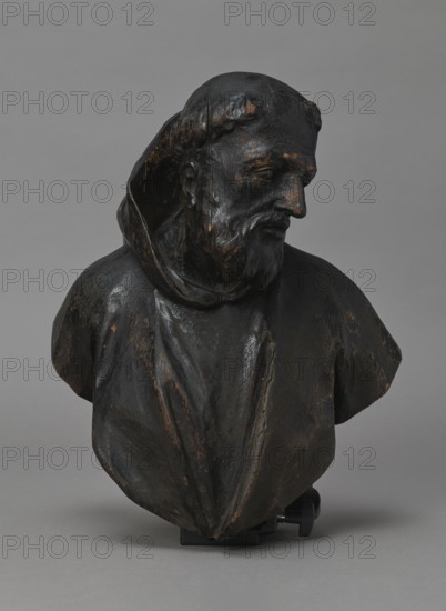 Bed finial, Redler, Jan Chryzostom 1704–1779 woodcarver; author, Fontana, Jakub 1710–1773 designer; co-creator; baroque; HOSPITAL BED FINIAL in the form of a pediment with volutes on the sides and a corbel in the middle supporting the bust of a monk; fastened with two pins to the front section of the cornice crowning the canopy. Figure dressed in a habit, with head turned to the left, with tonsure and beard. Outline of the finial and corbel highlighted with a black ribbon stucco inlay. On the corbel, an oval hole filled with a wooden, rotating medallion with inlaid letters on the obverse and reverse missing; above it, inlaid number No. i3. On the runners are garlands made of ribbons, flowers, and acanthus leaves; on the volutes are small brackets with turned, cup-shaped pinnacles. ca. 1757–1760, Warsaw; fragment of furniture; height 69.5 cm, width 91 cm, depth 24 cm, A dark wooden bust of a bearded man wearing a hooded garment is shown against a neutral gray background, with visible wo...
