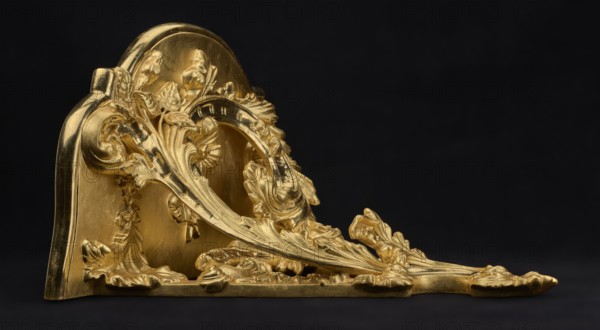 Hanging console, acanthus ornament, floral ornament, rococo style, ca. mid-18th century, Central Europe, piece of furniture; height 37.3 cm, width 41.5 cm, depth 26 cm, A decorative metallic object with ornate leaf and floral motifs rests against a dark background; the object has a polished golden surface with reflected highlights and shadowed recesses, featuring flowing curved shapes, sculpted petals, curling acanthus-like leaves, raised ridges, and smooth rounded sections; a flat base supports the sculptural elements and a curved back plate rises behind the ornamental scrolls; colors visible are gold, black, and subtle variations of darker gold where shadows appear.