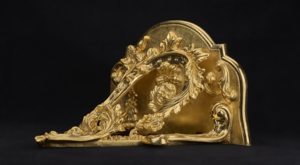 Hanging console, acanthus ornament, floral ornament, rococo style, ca. mid-18th century, Central Europe, piece of furniture, height 37.3 cm, width 41.5 cm, depth 26 cm, A decorative metallic object with ornate, raised floral and scrollwork designs in a bright gold tone sits against a dark black background, showing a curved backplate and an angled front element with flowing leaf and flower motifs, glossy highlights and subtle shadowing accentuating the sculpted details and smooth surfaces, with visible areas of polished shine and softer matte gold, all resting on a flat dark surface.