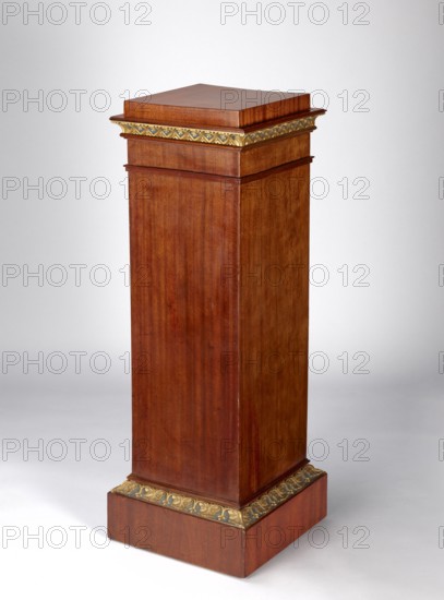 Pedestal cabinet, single-leaf with a drawer at the top, supported by a prominent plinth; veneered with mahogany, with profiled, carved, gilded and painted cornices and applied decoration on the doors. The edges of the door leaf and drawer faces and the corresponding front edges of the walls are diagonally cut. The molding around the plinth is decorated with a dark green and gilded leaf ornament; the cornice under the top is decorated with rosettes set in a rhomboidal grid. The upper section of the door features a bas-relief woman's head, below it a lotus flower surrounding the keyhole; the drawer face has a gilded wooden handle in the shape of a mushroom. Originally four shelves inside; the drawer bottom is recessed from the back. A single-bolt, self-locking steel mortise-and-apply lock and brass pintle hinges. Empire style; first quarter of the 19th century; possible origin Poland or Austria. Height 97.2 cm, width 33.5 cm, depth 35.2 cm., A tall wooden pedestal with a rectangular colu...