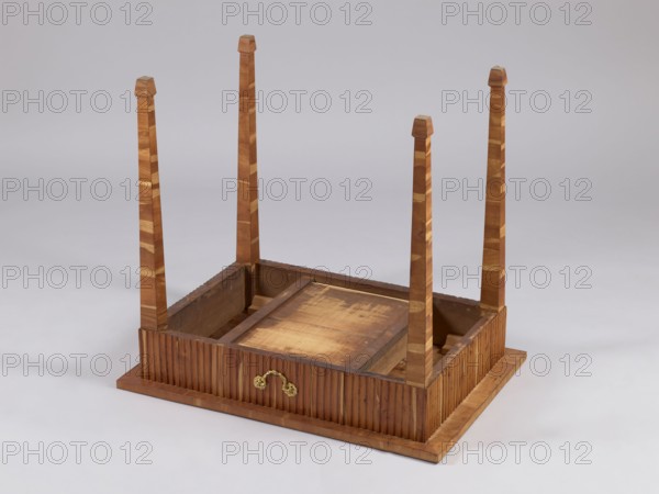 Table, snakes, rosettes ornament, plant decoration, classicism style, rectangular table with a drawer in a fluted frame, supported by four straight, angular, tapering legs terminating at the bottom in wedge-shaped feet. Entire piece veneered with rosewood and polished. Tabletop has a straight, plate-shaped rim, veneered in a cross pattern, with a rectangular central field and a narrow cross-frame, blintzed on the underside. Drawer handle in the form of a knob made of twisted rope with rosette plates. Drawers form a glued frame with sockets in the corners for mounting the leg tenons. Late 18th century, possibly Warsaw. Furniture, table. Height 76.5 cm, width 84.2 cm, depth 59.5 cm., An upside-down wooden table with a rectangular base and four tall, tapered legs pointing upward, the wood showing a mix of light and medium brown tones with visible grain and alternating lighter inlays on the legs; the base has vertical ridged paneling around its sides in a darker brown, a small brass-colore...
