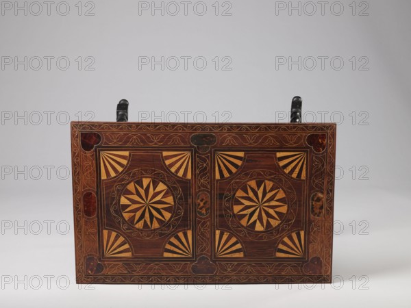 Table, geometric decorations, plant ornaments, rectangular table supported by four straight, spiral legs tilted outwards and sideways, joined at the bottom with an H-shaped tie and at the top with cross stiles connecting them in pairs. Cubes are located at the foot of the table. The tabletop is inlaid and covered with plant twigs and fans oval in the middle, quarters of an oval in the corners, halves halfway along the long sides; with a straight rim decorated with a wave motif. Type: Baroque-style furniture from the 2nd half of the 19th century. Date: 17th century, ca. 1660–1690. Possible origin: Spain or Flanders. Object: piece of furniture, table. Dimensions: height 56.5 cm, width 83.7 cm, depth 53.8 cm., A rectangular wooden panel with intricate geometric inlay occupying most of the image, showing a symmetrical design composed of two adjacent square sections each containing a circular starburst motif in lighter wood set against darker wood, surrounded by quarter-circle fan patterns ...