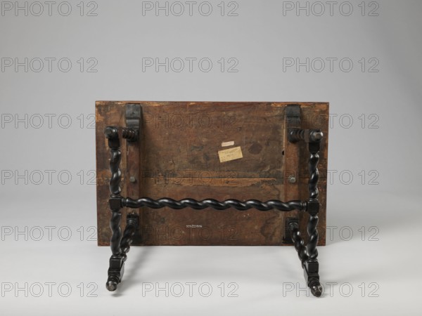 Table, geometric decorations, plant ornaments, rectangular table supported by four straight, spiral legs tilted outwards and sideways, joined at the bottom with an H-shaped tie and at the top with cross stiles connecting them in pairs. Cubes are located at the foot of the table. The tabletop is inlaid and covered with plant twigs and fans oval in the middle, quarters of an oval in the corners, halves halfway along the long sides; with a straight rim decorated with a wave motif. Baroque-style furniture from the 2nd half of the 19th century; dated to 17th century, ca. 1660–1690; Spain, Flanders ; piece of furniture, table; height 56.5 cm, width 83.7 cm, depth 53.8 cm., A wooden table viewed from the underside showing a rectangular top with worn, dark brown wood and a few areas of lighter brown wear; attached to the top are turned, twisted legs and stretchers finished in a glossy black, with a group of twisted horizontal and vertical supports forming the base; metal fasteners are visible ...