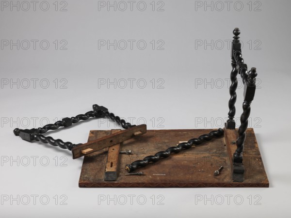 Table, geometric decorations, plant ornaments, rectangular table supported by four straight, spiral legs tilted outwards and sideways, joined at the bottom with an H-shaped tie and at the top with cross stiles connecting them in pairs. Cubes are located at the foot of the table. The tabletop is inlaid and covered with plant twigs and fans oval in the middle, quarters of an oval in the corners, halves along the long sides; with a straight rim decorated with a wave motif. In the type of Baroque furniture from the 2nd half of the 19th century. 17th century, ca. 1660–1690, Spain, Flanders, piece of furniture, table, height 56.5 cm, width 83.7 cm, depth 53.8 cm, A flat rectangular wooden board with a worn brown surface sits on a light gray background, with a few dark brown and black wooden pieces arranged on and around it; there is a group of twisted, spiral-shaped black wooden posts, a few straight wooden slats in natural brown tones, and a couple of small metal screws and fittings with a ...