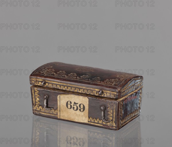 Case for a stamp, bookbinding, embossing; leather case in the form of a chest slightly widened at the top, with an eternal hinge slightly convex, covered with leather with gold-embossed decoration stripes and zigzag lines at the edges; on the lid, flowers with stems at the edge and one in the center. Interior lined with pink satin. 2nd half of the 18th century, Poland . Case; height 3.5 cm, width 7.8 cm., A small rectangular box with a domed lid sits on a reflective surface, showing a dark brown leather-like finish with decorative floral embossing on the top and gold-colored ornamental borders along the edges; the front and sides feature metal loop handles and corner embellishments, and the overall color palette includes dark brown, gold, beige, and hints of gray and reddish tones.