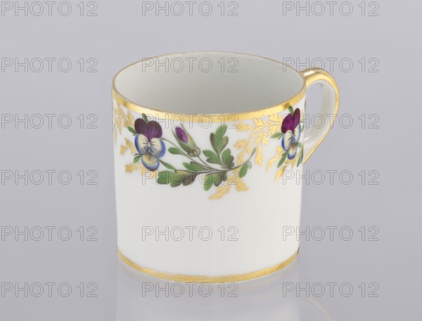 Cup with pansies, Korzec Porcelain and Faience Manufactory, 1805–1821. Cylindrical cup litron with a trail of gilded twigs and colorful pansies around the upper part of the bowl under the rim; gilded rim and loop handle. Porcelain, height 6.1 cm, width 8.8 cm, diameter 6.5 cm. Origin: Korzec, Volhynian Governorate., A white porcelain cup with a gold rim and gold band near the base, decorated with a painted floral garland featuring green leaves, purple and blue flowers, and gold leafy accents, and a gold-accented handle against a pale gray background.