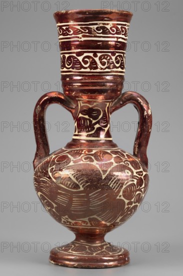 Amphora-type vase, Manises ceramic center; ca. 1400- author's role classification, pottery workshop author; mirrors decoration, birds, plant decorations. A slender, two-handled vase resembling a small amphora with a wide, long neck ending in a cup, and prominent, cylindrical, semicircular handles. The spherical body rests on a low spool foot. Painted with red mirror on a white background, with irregular patterns including a motif of exotic birds called pardalots and plant ornamentation. Horizontal trails with volute ornament on the neck. 17th century, Spain; Valencia; Manises. Vessel; height 26.5 cm, width 13.0 cm., An ornate vessel with a rounded body, a narrow neck flaring to a wide rim, and two curved handles rising from the shoulder to the neck, all decorated with carved or painted swirling and wave-like motifs; the surface shows a reflective, metallic sheen in deep reddish-brown and copper tones contrasted with lighter cream-colored areas where the decorative patterns appear, and ...