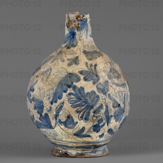 Bottle, Montelupo ceramics centre; ca. 1400–, pottery workshop, spherical bottle narrowed at the top with a pressed rim, foot slightly widening at the base. White earthenware painted with cobalt of varying saturation, loosely scattered plant motifs resembling oak leaves, flowers, and acorns. On the front of the body, a coat of arms cartouche under a banderole no inscription. The blue-and-white leaf decoration shows Venetian influence. 2nd half 16th century, Italy; Montelupo. Vessel; height 24.5 cm, width 18.0 cm., A rounded ceramic vessel with a narrow neck and chipped rim sits against a plain gray background; its surface is off-white with a crackled texture and decorated with a floral and leafy pattern painted in shades of blue, with areas of darker blue brushwork and faint grayish-blue outlines, and some brownish stains and worn spots around the rim and base.