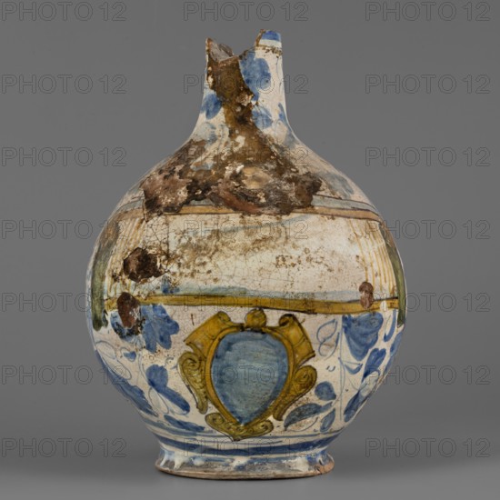 Bottle, maker, Montelupo ceramics centre; ca. 1400–, pottery workshop, plant decorations, cartouches, bottles. Spherical bottle, narrowed at the top with a pressed rim, the foot slightly widening at the base. White earthenware painted in cobalt of varying saturation with loosely scattered plant motifs resembling oak leaves, flowers, and acorns. On the front of the body, a coat of arms cartouche under a banderole no inscription. The blue-and-white leaf decoration shows Venetian influence. 2nd half 16th century, Italy; Montelupo. Vessel. Height 24.5 cm, width 18.0 cm., A rounded ceramic vessel with a narrow broken neck, showing surface wear and encrusted brown deposits, painted primarily in white with blue and yellow decorative motifs; there are a few areas of brown discoloration and cracking on the surface, a band of yellow encircling the body, a central shield-like decorative element in blue framed by yellow, and scattered blue floral or foliate brushstrokes around the lower half, all ...