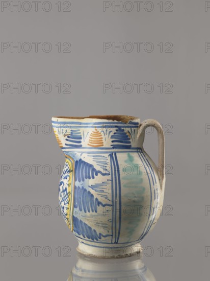 Jug, Orvieto ceramic center; 1450-, 16th century, Italy. Bulky jug with an ovoid belly on a low conical foot, with a wide, high cylindrical neck and a prominent triangular spout. Wide, ribbon-shaped vertical handle. Painted in cobalt and ochre with geometric and plant patterns. Front, under the spout: circular schematic rosette in cobalt alla porcellana—four-petalled leaf-flower with symmetrically arranged branches and rhombuses with double cross-stitching. On both sides of the reserve, highlighted by a yellow and ochre border, three zigzag rays in the form of flames surrounding the trigram of St. Bernard. Back: vertical stripes of green zigzags. Around the edge: trail of triangular hatching in alternating cobalt blue and ochre. Base unglazed. Subject: saints; Bernardine of Siena Saint; 1380–1444. Vessel. Height 20 cm, width 17 cm, depth 17 cm., A ceramic pitcher with a rounded body, a curved spout, and a single handle sits against a plain gray background; the pitcher is predominantly ...