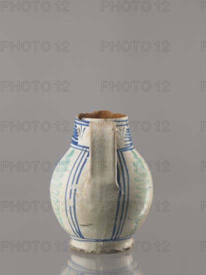 Jug, Orvieto ceramic center; 1450– Classified as a jug. Bulky jug with an ovoid belly on a low conical foot, wide high cylindrical neck and prominent triangular spout. Wide, ribbon-shaped vertical handle. Painted in cobalt and ochre with geometric and plant patterns. Front under the spout: circular schematic rosette in cobalt alla porcellana style—a four-petalled leaf-flower with symmetrically arranged branches and rhombuses with double cross-stitching. On both sides of the reserve, highlighted by yellow and ochre borders, three zigzag rays each in the form of flames fiamme surrounding the trigram of St. Bernard. Back: vertical stripes of green zigzags. Rim: trail of triangular hatching in alternating cobalt blue and ochre. Base unglazed. 16th century, Italy; Orvieto. Vessel. Height 20 cm, width 17 cm, depth 17 cm., A ceramic pitcher with a rounded body and a narrow neck, featuring a single vertical handle down the front; the surface is mostly off-white with painted blue linear pattern...