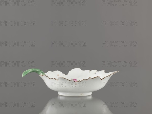 Leaf-shaped bowl, porcelain. Maker: Gardner, Francis porcelain factory; 1766-1917 and Wierbilki/near Moscow porcelain factory; 1766- . Leaf-shaped bowl on a ring-shaped foot. Rims cut in the shape of leaves with a triangular rim; opposite side a handle in the form of a green stem with veining. At the bottom a bouquet with a large purple-pink flower and three small floral motifs. Four cracks extending from the rim; glaze abrasions. Date: 1775–1800. Place: Russia, Wierbilki. Dish. Height 9.5 cm; width 12.0 cm., A shallow white porcelain dish with a scalloped, ruffled rim edged in a darker color sits centered on a reflective surface against a solid gray background; a curved green handle extends from one side, and a small hint of pink glaze is visible inside the dish.