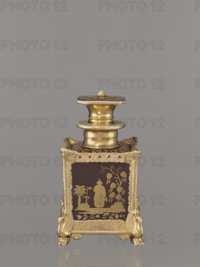 Bottle with lid. Porcelain manufactory of Francis Gardner 1766–1917. Chinoiserie cubic bottle with a profiled short neck and square stopper. Plastic ornamentation on the edges; swan-shaped feet in late Empire style one paw fragment missing. Gold-painted decoration with four genre scenes of Chinese people on the four sides; floral ornament on top of bottle and stopper; gilding abrasions. c. 1840, Russia; Wierbilki. Vessel. Height 18.5 cm; width 11.2 cm., A small ornate metal container stands against a plain gray background, featuring a polished gold-toned finish and a square body with a decorative lid and neck. The body sits on a base with four stylized feet shaped like animal paws, each foot and the frame around the panels showing intricate raised scrollwork in gold. Each visible panel has a dark brown background with a gold decorative scene depicting a standing figure in traditional attire beside stylized trees and foliage, framed by a gold border with repeating curved motifs. The lid...