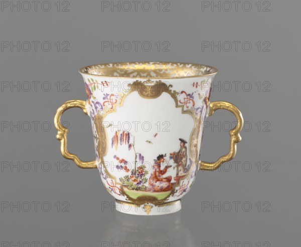 2-handled cup, Koenigliche Porzellain Fabrique, Meissen ca. 1720–1735, Hoeroldtmalerei. Chalice-shaped cup, slightly parted rim, rimmed foot, with two 2-part S-shaped gilded handles. Two 4-part gilded cartouches on the bowl, bordered by a purple-brick-red pincer ornament, with polychrome miniatures of genre scenes with Chinese figures and accompanying plant motifs and insects: 1 Chinese woman seated on a stool holding a fan and an incense burner with two Chinese children nearby; 2 tea ceremony scene: kneeling Chinese man with a cup and a standing man pouring from a teapot, beside fragments and a table with utensils. Upper handle sides and under the lower base decorated with shoots of Indian flowers. Inner edge with a trail of gold lace. Saxony, Meissen. Cup; height 7.8 cm, diameter 7.5 cm., A white porcelain double-handled cup with ornate gold handles and gold trim around the rim, decorated with delicate painted scenes and floral motifs in colors including purple, pink, red, green, ora...