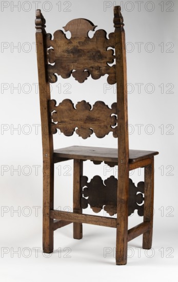 Chair, carved, reclaimed, volutes ornament, Renaissance style. CHAIR with a board seat and a high backrest composed of two boards with a wavy, openwork edge, supported by four straight, angular legs, the rear ones merging into slightly rearward-sloping backrest stiles. Legs fastened with casement binding with angular joints; front legs additionally joined at mid-height by a decorative board shaped analogously to the backrest boards carved with C- and S-shaped acanthus leaves, with single rectangular fields framed with inlaid veining. Side frames angular and narrow; front carved with a lower outline repeating the edge of the backrest boards and front legs. Seat edge profiled as a half-cylinder with a step. Finials of the side backrest frames in the form of a volute. Early 17th century; 4th quarter of the 19th century. Southern Germany ; Lombardy . Piece of furniture, seating piece. Height 121.5 cm; width 51 cm; depth 45.2 cm., A tall wooden chair with a high back featuring decorative cu...