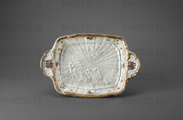 Sweets plate by Johann Joachim Kaendler 1706–1775 and Johann Friedrich Eberlein 1695–1749; Koenigliche Porzellain Fabrique, Meissen Meissen, Saxony, Swan Service. Rectangular, on four volute legs, with shell handles on the shorter sides, bearing the Brühl marital coat of arms. At the bottom a relief with swans, a crane and a heron; inner sides with shell relief, Indian flowers and gilded edge. Porcelain, 1740. Vessel; height 8.5 cm, width 31.0 cm, depth 20.4 cm., A shallow rectangular ceramic dish with curved handles sits against a neutral background; the dish is predominantly white with glossy surface textures and embossed radial and organic patterns, and it has gilded rims and handle edges in a gold color; small floral motifs in red, green, and orange appear around the interior edge and on the handles, and the handles also feature detailed multicolored decorative emblems with brown, blue, and red tones; the background is a smooth gray.