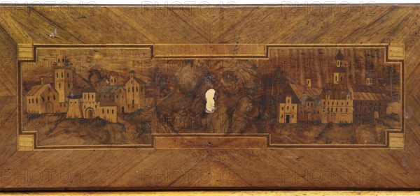 Chest of drawers, revindication provenance, roses, classicism style, vedute, geometric ornament, dolphins, eagles, rosettes ornament, ca. 1790, Saxony, piece of furniture, storage piece, height 97 cm, width 143 cm, depth 62 cm, A rectangular wooden panel with a framed central inlay depicting a landscape scene of a village, showing a group of buildings with towers, arches, and pitched roofs on rolling ground; the inlay shows several trees and a few clusters of foliage scattered among the structures, and a group of small birds drawn in the sky; the wood grain varies across the panel with darker and lighter brown tones and visible knots and a pale irregular worn spot near the center; the frame and inlay borders are in a slightly lighter brown with narrow darker trim, and the overall colors visible are shades of brown, tan, and a little black used for fine details.
