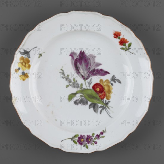 Shallow plate, Churfuerstliche Porcellain Fabrique, Meissen Marcolini period, 1774–1814; maker’s classification/manufacture noted; attributed to Meissen 1763/74–1814. Porcelain shallow plate with a 12-leaf collar and wavy edge with an ochre border. In the central mirror: a bouquet with a raspberry tulip, forget-me-nots and bells. On the collar: three floral patterns; leaf projections; some flaws. Black-painted ownership mark on the bottom: SAR./K., dated 1774–1814. Associated inscription: Stanislaw August Poniatowski King of Poland; 1732–1798. Country of origin: Germany. Vessel., A round white ceramic plate with a scalloped rim and a thin brown edge, decorated with a central floral arrangement featuring a large purple and white tulip-like flower, green leaves, a red-orange round flower, and a yellow blossom, all accompanied by grayish foliage and small pale blossoms; additional small floral sprays appear near the rim in yellow with dark gray leaves, orange with green leaves, and purple...