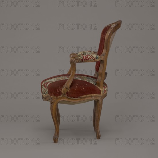 Armchair, rococo, flowers, geometric ornament, ca. 1760, France; seating piece piece of furniture; height 85.5 cm, width 62 cm, depth 60 cm., A wooden chair with curved legs and carved arm supports upholstered in deep red velvet and patterned fabric, showing some worn areas; the wood is a warm brown with visible grain and smooth finish; the upholstery includes colors such as red, beige, green, and blue; the chair is photographed against a uniform gray background.