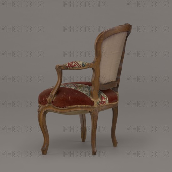 Armchair, rococo style, flowers, geometric ornament, ca. 1760, France; piece of furniture, seating piece; height 85.5 cm, width 62 cm, depth 60 cm, A wooden armchair with a curved back and cabriole legs upholstered in worn red fabric and patterned woven fabric on the seat and armrest; the backrest shows an exposed pale beige lining on its rear, and the wood has a medium brown finish with visible wear and small scratches; colors visible include red, beige, brown, green, and blue, set against a neutral gray background.