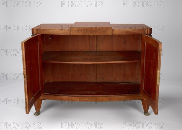 Cabinet, Empire style, mahogany veneered and polished, 1815–1825, possibly Warsaw. One-piece cabinet with a slightly rounded front closed by double doors, supported by four low angular tapering legs terminating in feet shaped like animal paws. Front corners chamfered with herm pilasters; top has a wide frame raised in the center and projecting like a cornice. Door leaves framed with single panels and cubes in the corners; back framed with two panels. Decor includes female busts, herm feet and leg slopes cast in cast iron; brass hinges. Height 83 cm, width 113 cm, depth 56.3 cm., A wooden cabinet with both doors open revealing an interior shelf and a lower compartment, the wood showing reddish-brown and lighter brown tones with visible grain and some wear, the top surface flat with a central raised rectangular section, the cabinet standing on short tapered legs with small decorative metallic feet that are a dark brass color, the doors panelled and hinged at the sides, and the background...