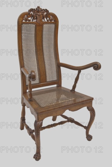 Armchair, creator unknown, provenance unknown, eagles, coats of arms, plant decoration, Neo-Baroque style, volutes, balusters, animal paws. Baroque armchair with carved frame, woven. Front cabriole legs ending in claws clasping balls, decorated at tops with acanthus leaves; rear legs in the form of balusters terminating with ankles. Legs fastened with an H stretcher composed of rolling joints, with ankles at the side. Trapezoidal seat with woven rattan and narrow frames with wavy cutouts at the bottom. High, nearly rectangular backrest, S-shaped at the back, with side rails curved toward each other at the top and topped with volutes. Between them, a two-field coat of arms supported by two eagles, beneath a visor with labrets and a hat above with a wide brim and two cords with tassels. Center of the backrest has a narrow central board dividing it into two fields woven with rattan mesh. S-shaped armrests terminate in volutes at the front and rest on straight, turned brackets set at an an...
