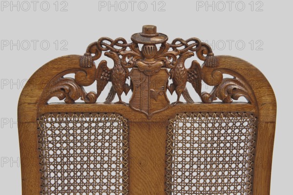 Armchair, provenance, Neo-Baroque, 2nd half of the 19th century, Western Europe. Baroque-style armchair with carved frame and woven rattan seat and back. Front cabriole legs terminate in claws clasping balls, decorated at the top with acanthus leaves; rear legs shaped like balusters terminating with ankles. Legs joined by an H stretcher with turned joints and side ankles. Trapezoidal seat with woven rattan and narrow frames with wavy cutouts at the bottom. High nearly rectangular backrest, S-shaped at the back, side rails curved inward at the top and topped with volutes. Center backrest divided by a narrow central board into two rattan-woven fields. Back crest features a two-field coat of arms supported by two eagles beneath a visor with labrets and a hat with wide brim and two cords with tassels. S-shaped armrests end in volutes at the front and rest on straight turned brackets set at an angle. Frame joints pegged. Furniture, seating piece; H 120 cm, W 70 cm, D 54 cm., A carved wooden...