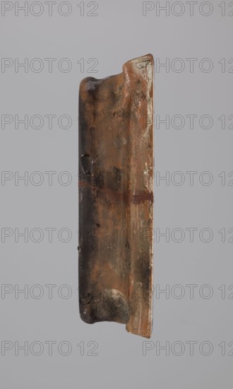 Tile, tiles, Hutsulshchyna, stoves, saints, 1851, with a representation of a saint, Hutsulshchyna, tile, height 23.7 cm, width 20.0 cm, depth 6.0 cm, An upright, elongated object with a rough, weathered surface showing a range of brown and rust tones, including dark brown, reddish-brown, and lighter tan areas, with patches of gray and small areas of off-white along one edge; the object has an irregular, slightly curved profile with worn, rounded ends and a shallow groove running vertically, plus a few darker spots and smudges and subtle shiny patches suggesting a glazed or polished finish against a plain light gray background.