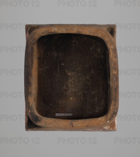Tile;, Ceramic tile decorated with plant motifs, Maltese crosses, crosses, and a depiction of two birds. Hutsul region, 19th century. Dimensions: height 20 cm, width 23 cm, depth 6 cm. Classification: tiles, stoves., A rectangular object with rounded inner edges viewed from above showing a dark, worn interior surrounded by a rim in shades of brown and tan, set against a light gray background; the rim has mottled patches of darker brown and lighter tan, and the interior surface appears textured with dark brown and black areas and some lighter brown spots.