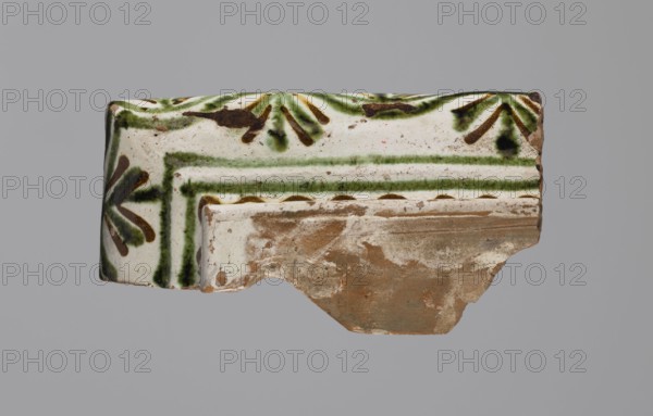 Cornice tile fragments four, tile cullet; painted with a wavy twirl pattern; 19th century; Hutsul region, Poland; plant decorations; stoves., A broken ceramic fragment with a glazed surface showing white, green, brown, and black colors; the glaze displays a decorative pattern of green lines and stylized brown and black leaflike shapes on a white background, with a band of green stripes and a row of brown semicircular marks; the unglazed underside is exposed and shows rough, earthy brown clay with patches of white residue and wear; the edges are irregular and chipped.