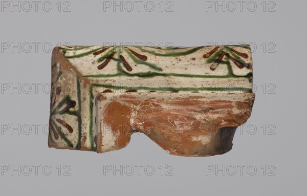 Cornice tile — fragments, four;, tile cullet; stoves; plant decorations; Hutsul region; fragments of a cornice tile painted with a wavy twirl pattern; 19th century; Poland., A broken ceramic fragment with a glazed surface showing white, green, brown, tan, and reddish-orange colors; the glaze includes green linear patterns and brown petal-like marks on a white background, with a worn reddish-orange terracotta area where the piece is fractured, and patches of tan and darker brown weathering visible across the surface.
