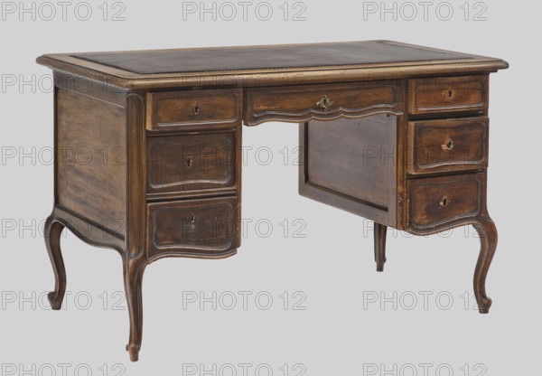 Desk, rococo style, cabriole legs, provenance unknown, 1880–1890, Vienna, piece of furniture, writing furniture, height 74 cm, width 119.5 cm, depth 67 cm, A wooden desk photographed against a pale gray background showing a warm brown finish with darker brown top inset and lighter brown edging; the desk has a rectangular top with a darker inset surface and a decorative molded edge, curved legs with scrolled feet, and a symmetrical arrangement of drawers on each side with recessed panels and visible keyhole openings, one central drawer with a small metallic decorative pull, wood grain and areas of wear visible across the surfaces, and an open knee space framed by a scalloped apron.