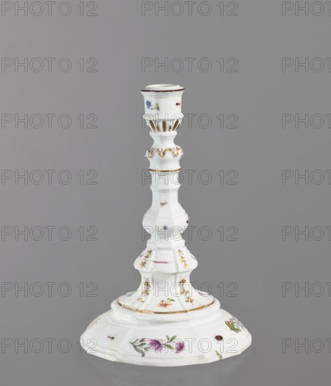 Candlestick, Koenigliche Porzellain Fabrique, Meissen 1710–1763. One-candle candlestick with profiled baluster shaft and 8-segment round foot; candle socket mounted on a profile with relief acanthus leaves. Decorated with gilding sleeve channels, acanthus frieze, gold-painted and relief campanulas and four sprigs of woodcut flowers daffodils, wood violets, forget-me-nots, and brick-red balls around the foot, between the campanulas, and on the socket; also small insects and bugs. Brown border around the edge of the candle holder. Ca. 1740–1745. Saxony, Meissen. Lighting. Height 24 cm; diameter 16 cm., A white porcelain candlestick with a flared circular base and a tall, tiered stem decorated with small painted flowers and insects in colors including purple, pink, blue, green, brown, and gold highlights; the piece shows molded ridges and scalloped edges, with gold trim accenting several raised bands and decorative flourishes, all set against a plain gray background.