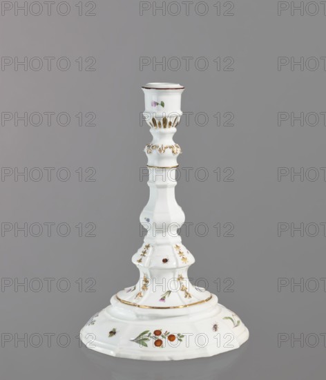 Candlestick, Meissen ca. 1740–1745. One-candle candlestick with profiled baluster shaft and 8-segment round foot; candle socket mounted on a profile with relief acanthus leaves. Decorated with gilding sleeve channels, acanthus frieze, gold-painted and relief campanulas and four sprigs of woodcut flowers daffodils, wood violets, forget-me-nots, and brick-red balls around the foot, between the campanulas, and on the socket; also small insects and bugs. Brown border around the edge of the candle holder. Porcelain; height 24 cm, diameter 16 cm. Origin: Meissen, Saxony., A single ornate white ceramic candlestick stands against a gray background, featuring a flared base with painted floral and fruit motifs in red, green, and orange, and small painted insects in brown and black; the stem is sculpted with curving, tiered sections accented with gold highlights and delicate painted flower details in pink and green, and the top has a cup-shaped holder with a thin brown rim.