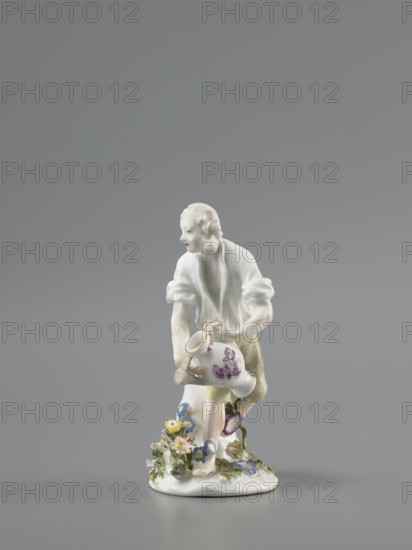 Gardener, Koenigliche Porzellain Fabrique, Meissen 1710–1763; Kaendler, Johann Joachim 1706–1775 sculptor? ; Reinicke, Peter 1715–1768 sculptor? ; gardeners, figurine. On a circular base with a high tree trunk and plastic tufts of flowers stands a slightly bent barefoot man, leaning against the trunk, in knee-length trousers and a luxurious shirt with rolled-up sleeves; he holds a watering can in his left hand, tilting it to water the flowers, and supports the spout with a strainer in the palm of his other hand. Ca. 1760. Meissen, Saxony, Germany. Porcelain figurine; height 12 cm., A small porcelain figurine of a person leaning forward, wearing a white top with rolled sleeves and pale yellow-green shorts, holding a white jug with purple floral decoration, standing on a white base adorned with a group of small colorful flowers in blue, yellow, pink, and green foliage against a neutral gray background.