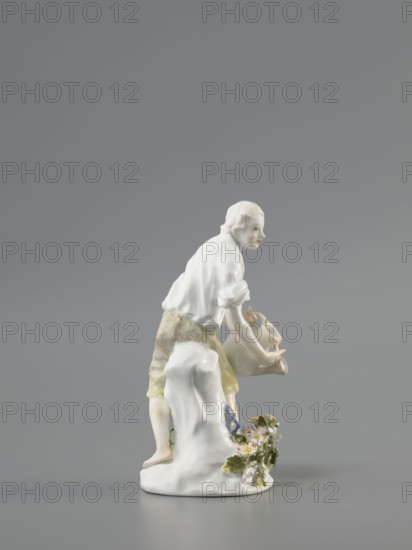 Gardener, Königliche Porzellan-Fabrique, Meissen 1710–1763; Kaendler, Johann Joachim 1706–1775 sculptor? ; Reinicke, Peter 1715–1768 sculptor?. On a circular base with a high tree trunk and plastic tufts of flowers stands a slightly bent barefoot man, leaning against the trunk, in knee-length trousers and a luxurious shirt with rolled-up sleeves; he holds a watering can in his left hand, tilting it to water the flowers, and supports the spout with a strainer in the palm of his other hand. Ca. 1760. Meissen, Saxony, Germany. Porcelain figurine; height 12 cm., A small porcelain figurine of a person leaning forward, shown in profile, with pale skin and light hair, wearing a white top and light yellow-green knee-length bottoms. The figure holds a pale jug or pitcher with both hands and stands with one foot on a white sculpted rock or mound. At the base near the rock is a cluster of painted flowers with green leaves and petals in white, pink, and blue. The overall background is a smooth gra...