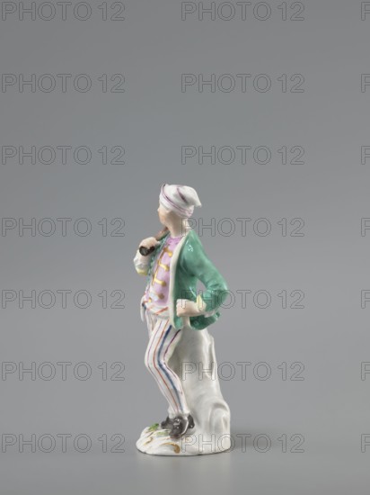 Man with a Potato Masher, Reinicke, Peter 1715–1768 modeler?, Koenigliche Porzellain Fabrique, Meissen 1710–1763 manufacturer, figurine. On a flat, circular pedestal with rocaille merging into a tree trunk, stands a young man leaning on the trunk at waist level. In contrapposto, head turned to the right, he holds a short oval board with a handle—an instrument for stewing potatoes—resting on his right shoulder. Dressed in trousers with colorful thin stripes tied loosely at the waist with a belt, with loose ends, black shoes with a buckle, a short green jacket with box pleats, a pink waistcoat, with gold braiding and a soft cap similar to a nightcap. Ca. 1755, Saxony; Meissen. Figurine, height 13.5 cm., A porcelain figurine of a standing person wearing a white cap with purple bands, a green jacket, a pink vest, and white trousers with vertical purple and blue stripes, posed with one hand on the hip and the other holding a small dark object near the shoulder, standing beside a white sculp...
