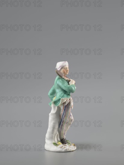 Man with a Potato Masher, Reinicke, Peter 1715–1768 modeler?, Koenigliche Porzellain Fabrique, Meissen 1710–1763 manufacturer, figurine. On a flat, circular pedestal with rocaille merging into a tree trunk stands a young man leaning on the trunk at waist level. In contrapposto, head turned to the right, he holds a short oval board with a handle—an instrument for stewing potatoes—resting on his right shoulder. Dressed in trousers with colorful thin stripes tied loosely at the waist with a belt, black shoes with a buckle, a short green jacket with box pleats, a pink waistcoat with gold braiding, and a soft cap similar to a nightcap. Ca. 1755; Meissen, Saxony. Figurine, height 13.5 cm., A small porcelain figurine of a standing person wearing a white head covering with a faint pink stripe, a green jacket, and baggy white trousers with vertical stripes in purple, orange, and blue, holding a brown object over one shoulder and leaning against a white textured support, standing on a white base...