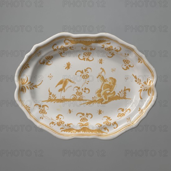 Platter, mid-19th century style referencing 18th-century France, Moustiers-Sainte-Marie ?. Oval platter with a four-leaf, wavy-edged collar. Painted in yellow with a genre scene and floral motifs. In the center, an arranged scene with a bawdy dwarf sitting on the grass, on the right, holding a hammer in his right hand. Opposite him stands a bird with spread wings, defending itself with its beak against the dwarf's blow. Remaining surface covered with plant motifs. On opposite edges are four leafy compositions, from two of which flowers and grasses grow. A more strongly marked part of the green ground for the dwarf and the bird. Around the edge is a triple yellow border. Vessel; height 3.0 cm, width 24.0 cm, depth 32.5 cm., A scalloped oval ceramic plate with a white base and mustard-yellow decorative painting, featuring a central scene of a seated childlike figure holding an object and a bird standing on the ground nearby, surrounded by stylized floral and foliate motifs and ornamental...