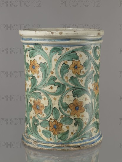 Vessel - flowerpot, unspecified manufacture, coats of arms, cartouches, cache-pot vessel, plant decorations. Vessel in the shape of a cylindrical flowerpot with profiled rollers at the base and spout. Decorated throughout with a motif of a stylized, fleshy plant twig in the form of an acanthus with flowers. On the forehead is a cartouche with the five-field coat of arms beneath a royal crown. The elaborate cartouche is supported by two lions rampant, with symbols of a griffin holding a pennant column?. Below the coat of arms is the date 1747. Green plant decoration with ochre flowers, blue cartouche shades ranging from navy blue to light blue. A hole in the bottom for draining water. 1747, Italy, Caltagirone, vessel, height 74 cm, width 31 cm., A cylindrical ceramic vessel with a glossy finish decorated overall with a repeating floral and foliate pattern in green and ochre with blue accents on a creamy off-white ground; the design shows curling green leaves and stems surrounding ochre ...