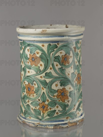 Vessel - flowerpot, unspecified manufacture; coats of arms; cartouches; cache-pot vessel. Cylindrical flowerpot with profiled rollers at the base and spout. Decorated throughout with a stylized, fleshy plant twig in the form of an acanthus with flowers. On the forehead is a cartouche with a five-field coat of arms beneath a royal crown. The elaborate cartouche is supported by two lions rampant, with symbols of a griffin holding a pennant. Below the coat of arms is the date 1747. Green plant decoration with ochre flowers, blue cartouche shades ranging from navy blue to light blue. A hole in the bottom for draining water. 1747, Italy, possibly Caltagirone. Vessel, height 74 cm, width 31 cm., A cylindrical ceramic vessel with a slightly flared rim and base, decorated all over with a repeating foliate pattern of stylized leaves and flowers; the surface shows a cream background with green scrolling leaves, orange flowers with blue centers, and small golden dot accents, and there are blue ba...