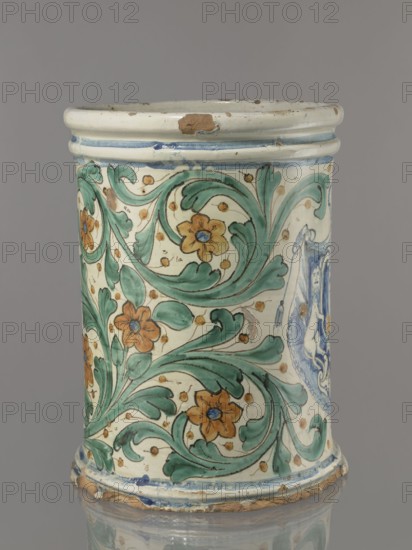 Vessel - flowerpot, coats of arms, cartouches, cache-pot vessel. Vessel in the shape of a cylindrical flowerpot with profiled rollers at the base and spout. Decorated throughout with a stylized, fleshy plant twig in the form of an acanthus with flowers. On the forehead is a cartouche with a five-field coat of arms beneath a royal crown. The elaborate cartouche is supported by two lions rampant, with symbols of a griffin holding a pennant column?. Below the coat of arms is the date 1747. Green plant decoration with ochre flowers, blue cartouche shades ranging from navy blue to light blue. A hole in the bottom for draining water. 1747, Italy, Caltagirone . Vessel, height 74 cm, width 31 cm., A cylindrical ceramic vessel with a glossy cream background decorated with a swirling botanical pattern in green leaves and orange flowers with blue centers, accented by small ochre dots; the rim and base show wear with exposed brown clay and chips, and there are blue painted bands near the top and b...