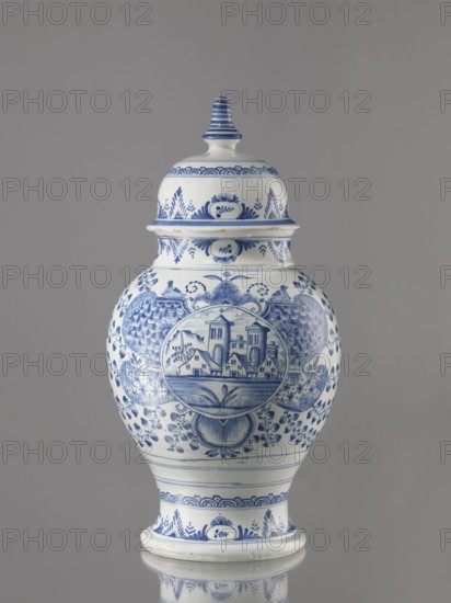 Vase with lid, Fayence-Manufaktur Muenden faience factory; 1732–1854 Hannoversch Münden, architecture, Méyet, Leopold 1850–1912; birds, plant motifs. Baluster vase with a short, slightly flared neck, pear-shaped belly, on a conical foot, with a domed lid terminating in a conical handle. Around the lid, neck, and foot is a pattern of triple semicircles, fir-tree and oval plant motifs and borders. On the front, in a circular cartouche, an architectural view with two towers and three houses with gable roofs. The cartouche is topped with a plant palmette with a circular motif at the bottom and richly ornamented on both sides with a scale mosaic, Chinese latticework, double volutes, and two birds at the top. Branches with flowers, fruits or oak leaves radiate horizontally from the cartouche. On the back are small stars and a bipartite shoot motif. 3rd quarter of the 18th century, Germany; Hannoversch Münden. Vessel; height 41.8 cm, width 21.0 cm., A lidded ceramic jar with a bulbous body an...