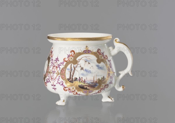 Lion's paw pot with miniatures, Königliche Porzellan-Fabrique, Meissen ca. 1730, Germany, Saxony — Whipped cream pot vessel with squat belly and wide collar around the rim; volute segmental handle gilded along the spine; on three legs shaped as lion's paws. Body with three oval/quadrangular reserves, each surrounded by a gilded frame with ovals of colorful Chinese latticework and purple-brick-red leaf motifs and Regency volutes — colorful landscape miniatures by the water with staffage: 1 a barrel-wheeler and four men at the quay, 2 two men with cargo at the shore and a woman and three men standing nearby, 3 four men waiting with luggage and sailing boats at the shore. Between the miniatures are two brick-purple Regency compositions with gilding; lion's paws and the outer edge of the collar are gilded. Maker: Meissen Königliche Porzellan-Fabrique, ca. 1710–1763 active date range noted., A white porcelain vessel with a flared rim and ornate handle sits on small feet against a neutral gr...